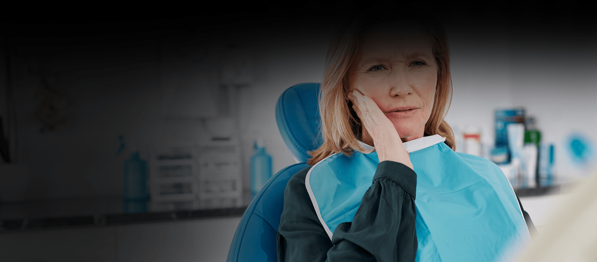 A woman holding her cheek in a dental chair